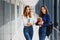 Two young women with book chatting while standing in college corridor. University students in corridor after the lecture