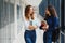 Two young women with book chatting while standing in college corridor. University students in corridor after the lecture