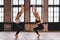 Two young women do complex of stretching yoga asanas in loft style class face to face. Chair Pose - Utkatasana.