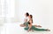 Two young women doing yoga indoor, sitting in position  over white studio background