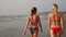 Two young women girlfriends are walking along the beach. Girls in bikinis on the sea