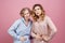 Two young women hold onto their bellies with suffering expression. Studio portrait on pink background.