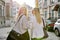 Two young women with laptop bags walking along street of sunset city, back view