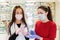 Two young women in medical masks and gloves on the background of a window with pharmacy products, consider the medicine. The