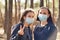 Two young women in medical masks look at camera in wood. Close up of females protecting yourself from diseases on walk