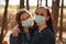 Two young women in medical masks look at camera in wood. Close up of females protecting yourself from diseases on walk