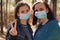 Two young women in medical masks look at camera in wood. Close up of females protecting yourself from diseases on walk