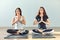 Two young women meditating in lotus pose with hands in namaste
