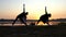 Two Young Women Practice Yoga And Bend Left on a Lake Bank at Sunset