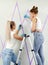 two Young women preparing wall for painting standing on ladder applying masking tape on wall. Diy project