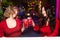 Two young women in red clothes drink cocktails and celebrate in a nightclub or bar. Women clink glasses