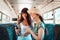 Two young women ride on public transport and cheerfully watch something on their smartphone. Concept of communication and social