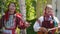 Two young women in Russian traditional dress stand under a birch tree and dance.