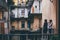 Two young women stand in patio together and look at it. Colorful windows in old city or town. Travel together.