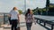 Two young women in street clothes are walking on the waterfront along the water.