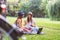 Two young women students in park sitting on grass talking, using laptop