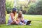 Two young women students in park sitting on grass talking, using laptop