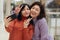 Two young women taking selfie with victory signs, looking at smart phone screen, being happy and expressing positive emotions,