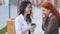 Two youthful attractive business womans, red-haired and brown-haired, talking and performing actions in smartphone