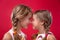 Twoloving sisters look at each other head-on and smiling on isolated red background. Close-up portrait of happy girls