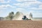 Typical agricultural scene tractor cultivation in field in clouds of dust drives off into the distance with birches