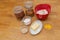 Typical baking ingridients for pastries like milk, butter, flour, nuts, egg yolk and sugar standing on wooden table in glasses and