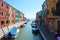 Typical brightly colored houses and narrow channels with tourists in Burano, Venice, Italy.