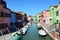 Typical brightly colored houses and narrow channels with tourists in Burano, Venice, Italy.