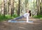 Typical caucasian girl in white sportswear does reverse plank exercise. Workout outdoor in the forest, in summer