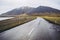 Typical dark gray wet asphalt of beautiful Icelandic roads. Highway by the lake and bold mountains covered by gray clouds. Pale