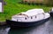 A typical dutch boat docked at a shore with grass and covered up under a white canvas