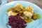 Typical german hearty meal: closeup of dumplings with brown sauce, red cabbage, goulash meat on blue china dish