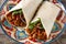 Typical Mexican burrito wrap with beef, frijoles and vegetables on wooden table.