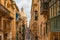 Typical narrow street of Valletta with Cathedral dome, yellow buildings and colorful balconies, Malta, Europe