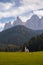 Typical scenery of small Church of San Giovanni in Ranui with dolomites Odle in background and clouds and foliage