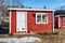 Typical small red colored guest house with one white door and white window at Swedish country side needs immediate renovation -