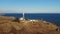 A typical striped lighthouse on the coast of the steppe area in the evening. Seashore steep aerial view