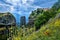 Typical view of Meteora, Greece, cliff monastery, sedimentary rocky pillars, yellow and poppy flowers. Sun rays fall