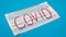 Typical white 3-ply surgical mask with rubber earhooks to cover mouth and nose with English block letters Covid on a blue