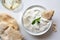 Tzatziki in white ceramic bowl with mint leaf garnish and a piece of pita bread next to pita bread and a glass of white wine from