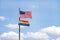 U.S. Flag flying in a blue cloudy sky with rainbow flag below blowing in the wind