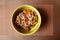 Udon stir-fry noodles with chicken and sesame seeds in green bowl on noisy brown background, on table mat. Top view