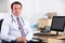 Uk doctor smiling at camera sitting at his desk