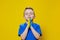 Ukrainian boy prays for Ukraine. Children against war. A boy in a blue T-shirt on a yellow background folded his hands