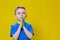 Ukrainian boy prays for Ukraine. Children against war. A boy in a blue T-shirt on a yellow background folded his hands