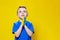 Ukrainian boy prays for Ukraine. Children against war. A boy in a blue T-shirt on a yellow background folded his hands
