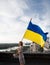 Ukrainian flag in hands of woman standing on roof of house in Kyiv. View of Dnieper River and roofs of buildings