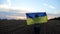 Ukrainian lady walking with national blue-yellow banner on barley meadow at sunrise. Woman going with raised flag of