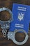 A Ukrainian passport with police handcuffs lies on a wooden table. Problems with the law during the crossing of the borders of co