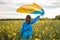 Ukrainian patriot woman waving national flag in canola yellow field. Rare, back view. Ukraine unbreakable, peace